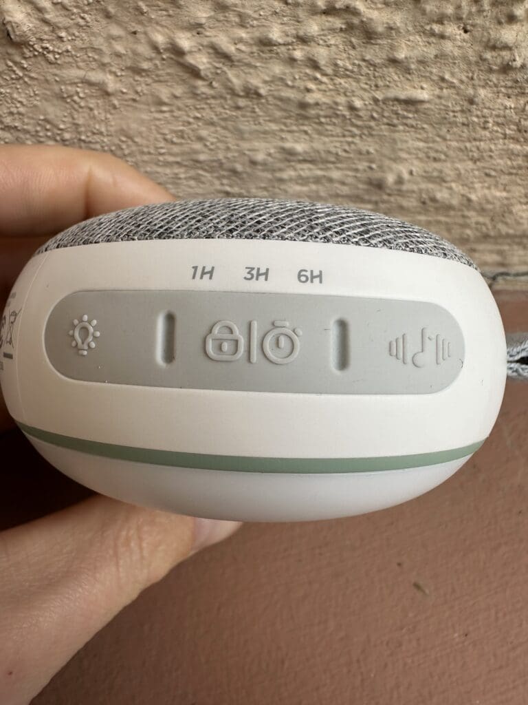 Momcozy Portable baby sound machine hand holding side view of light, timer and music buttons