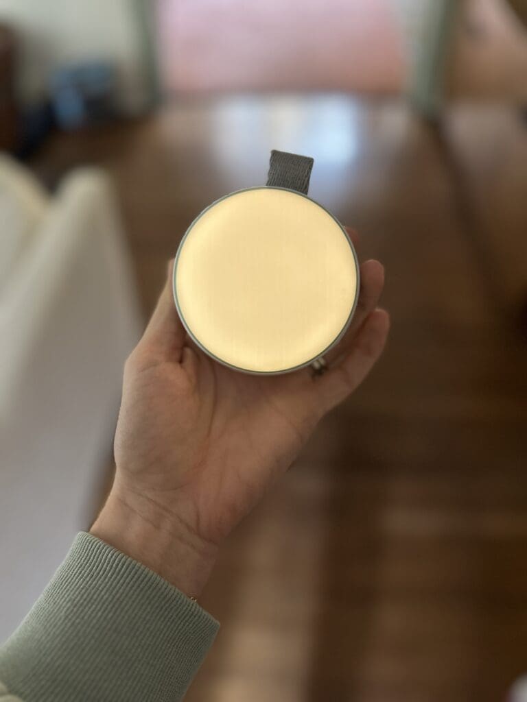 Momcozy portable baby sound machine hand holding it showing night light lit up