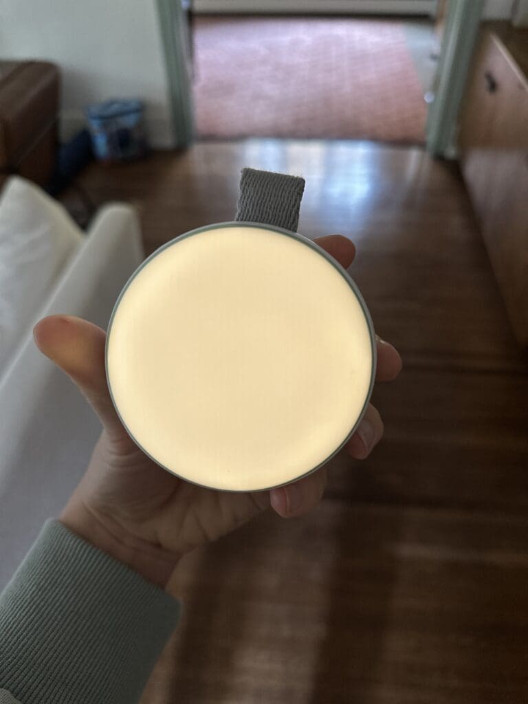 Momcozy portable baby sound machine hand holding device with nightlight lit up in dark