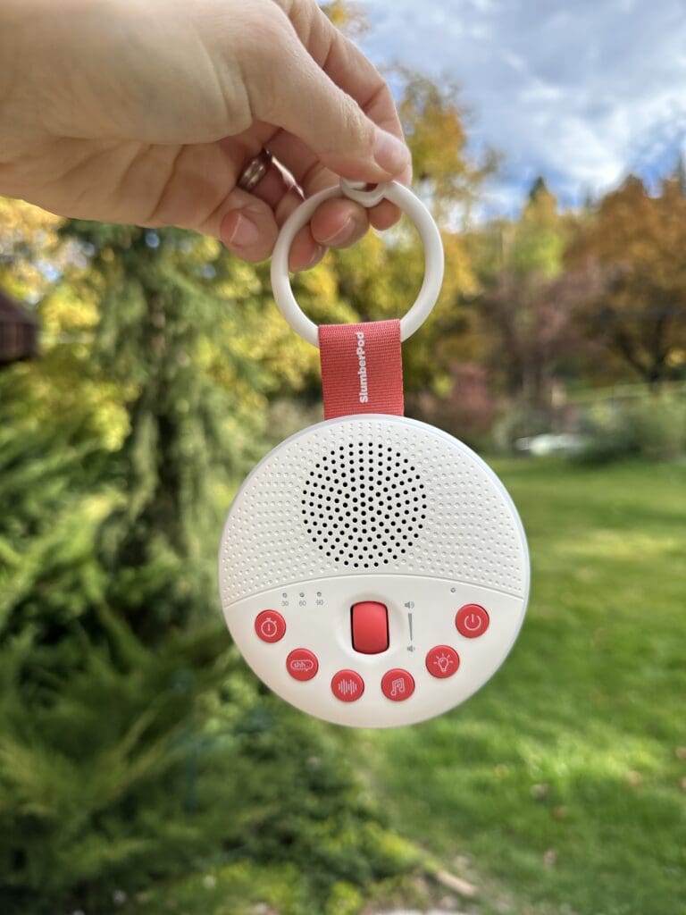 Hand holding SlumberPod SlumberCalm Portable Baby Sound Machine hanging outside