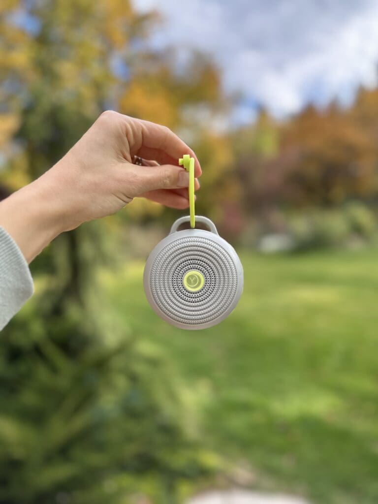 hand holding Yogasleep hushh portable baby sound machine outside showing how it dangles