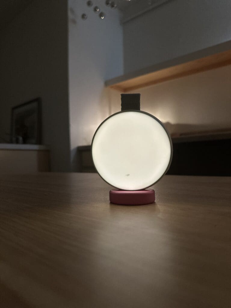 Momcozy portable baby sound machine sitting on desk with nightlight lit up in dark