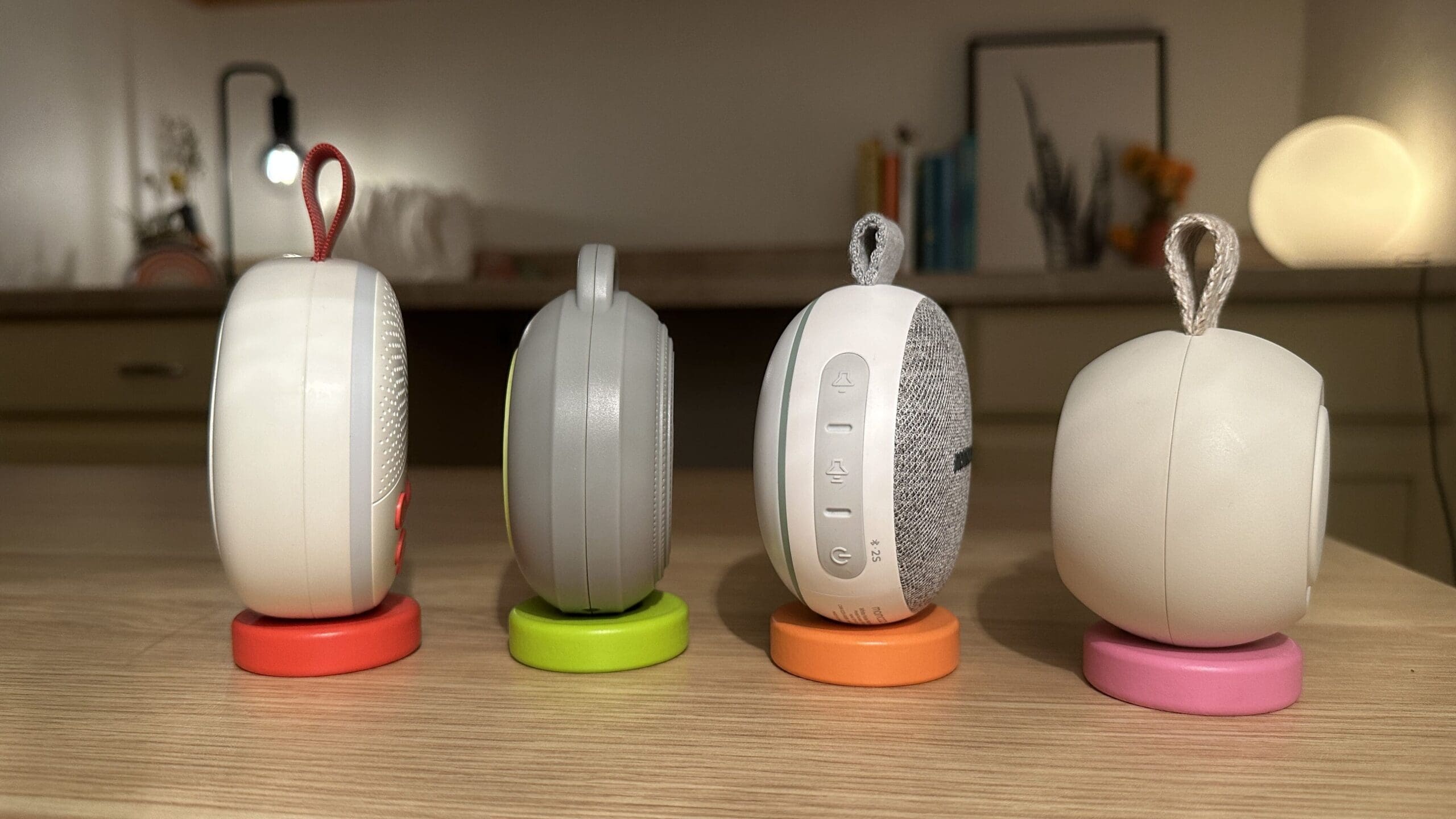 Side view of four portable baby sound machines up close front sitting on desk (SlumberPod SlumberCalm vs. Yogasleep Hushh vs. Momcozy Portable vs. Hatch Go)