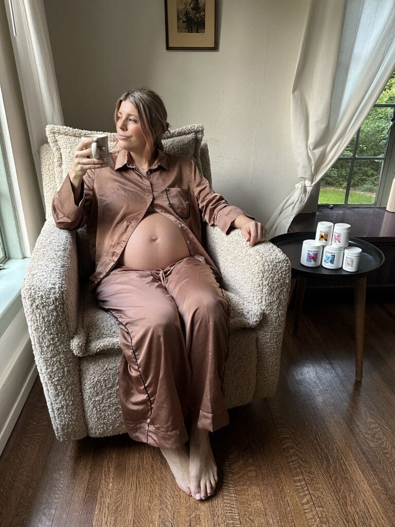 Pregnant Woman Drinking Coffee in Nursery Chair With Prenatal Stack Next To Her